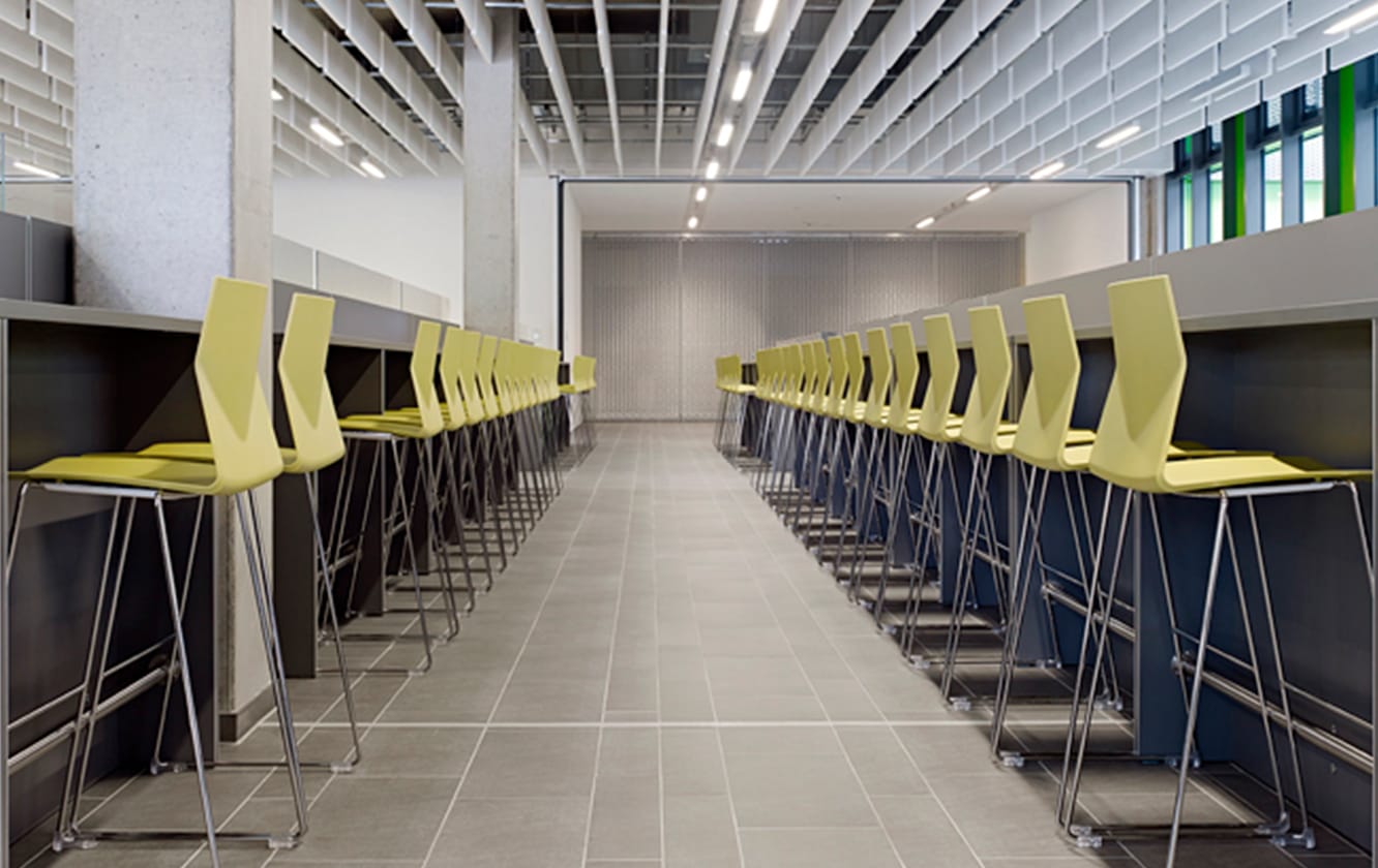 A long line of yellow counter chairs against bars in a modern office.