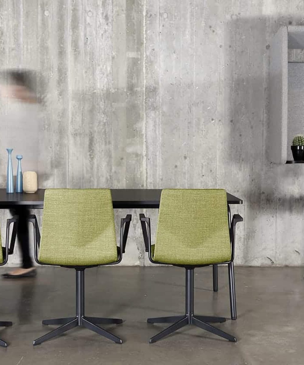 A table and chairs in a room with a concrete wall with a wall mounted desk workstation on the wall.