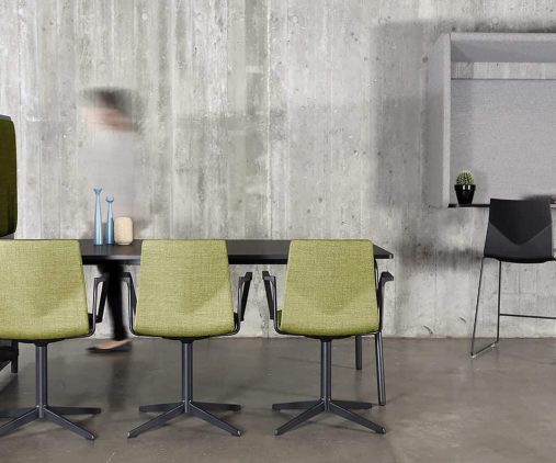 A table and chairs in a room with a concrete wall with a wall mounted desk workstation on the wall.