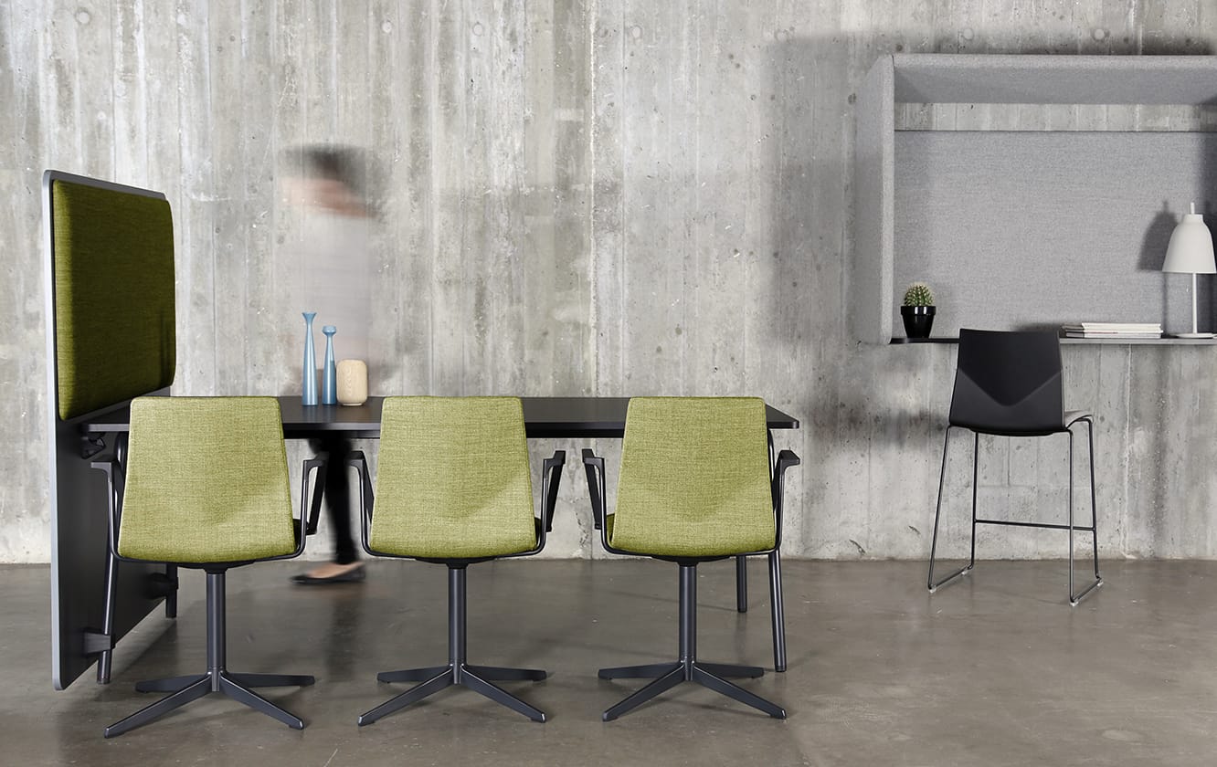 A table and chairs in a room with a concrete wall with a wall mounted desk workstation on the wall.