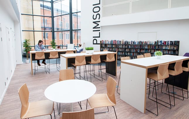 A library with standing height tables and chairs in the middle of the room.