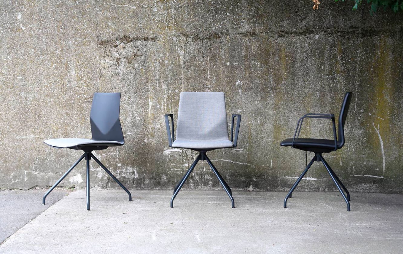 Three office desk chairs in front of a concrete wall.