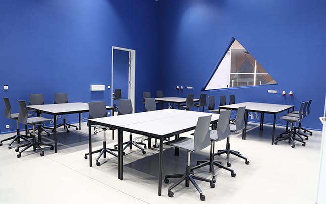 A classroom with tables and office desk chairs in a blue room.