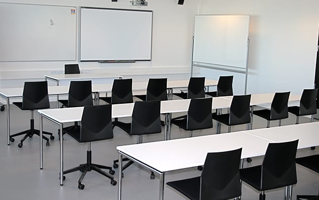 A classroom with black office desk chairs and a white board.