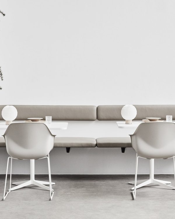 Wall mounted office benches next to white tables and chairs with a plant in the middle.