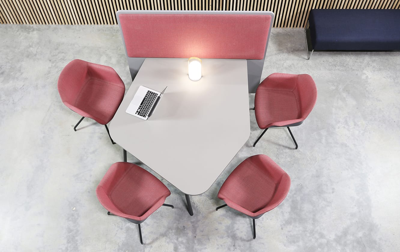 A table with an office screen divider with pink chairs and a wall behind it.