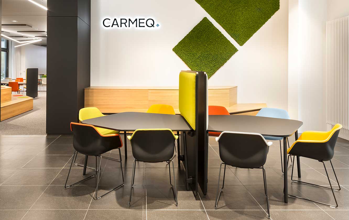 An office with a office tables with a office screen dividers between them and chairs and a green wall.