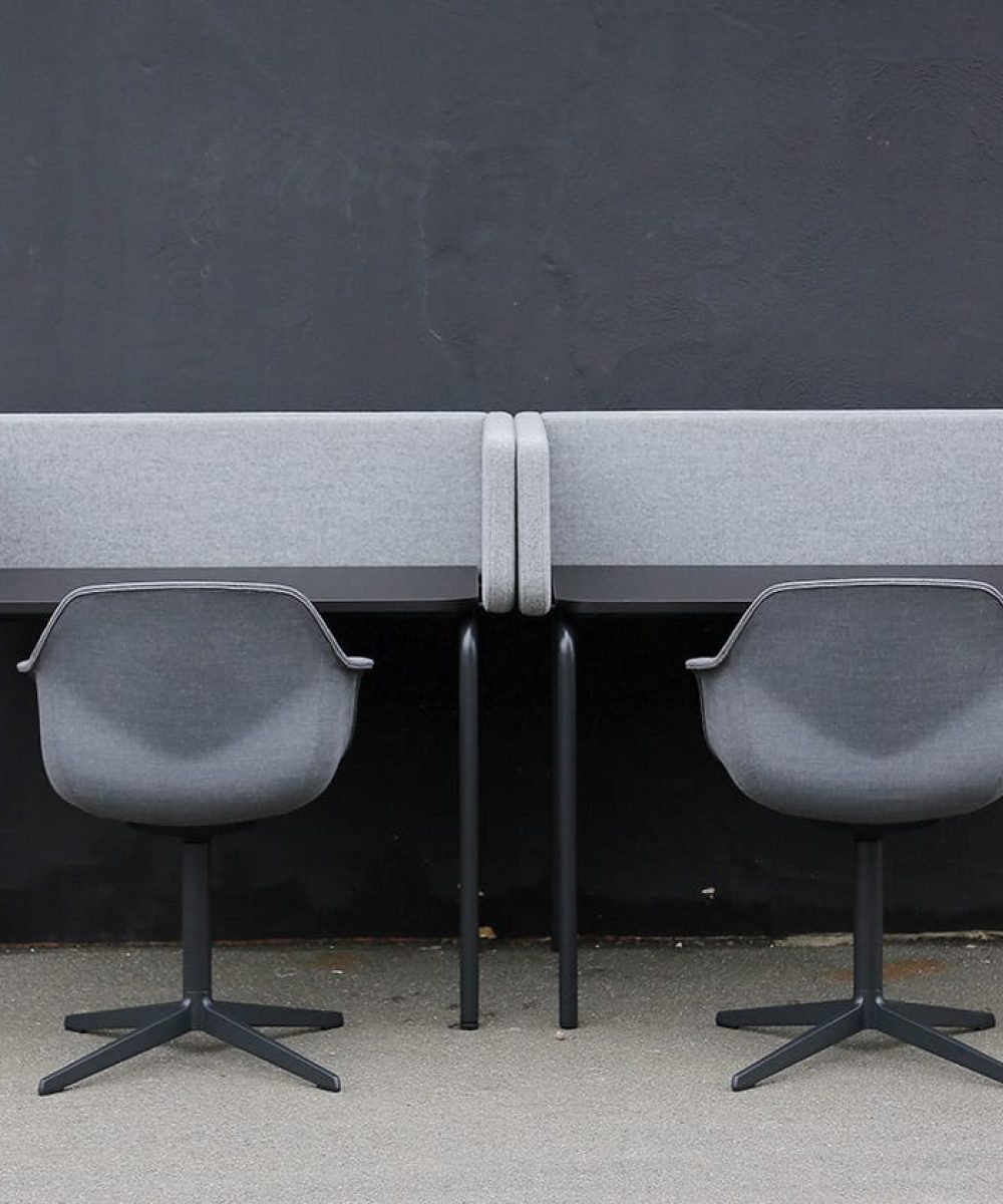 Two grey chairs in front of desk workstations in front of a black wall.