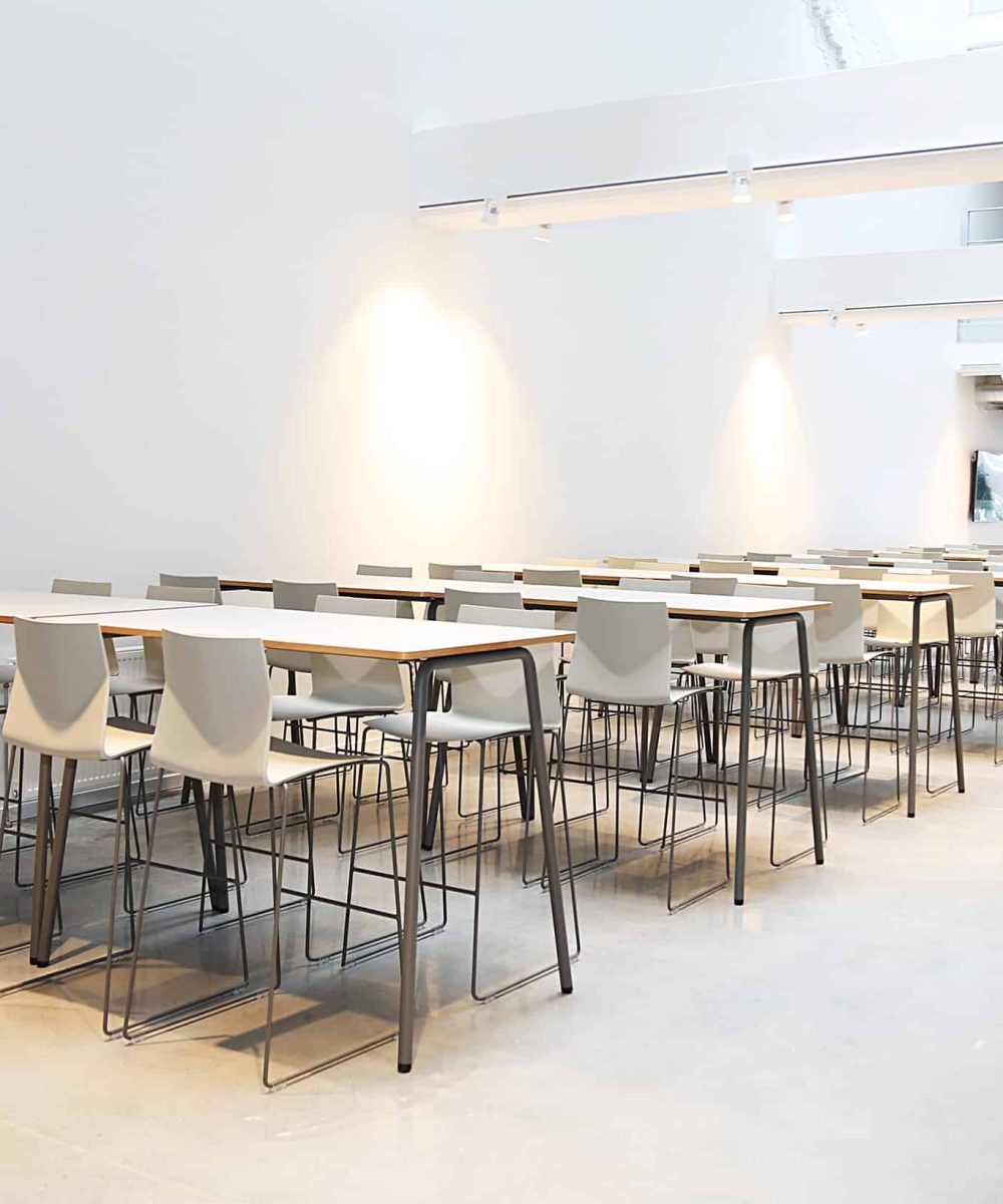 A large room with white standing height tables and chairs.