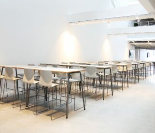 A large room with white standing height tables and chairs.