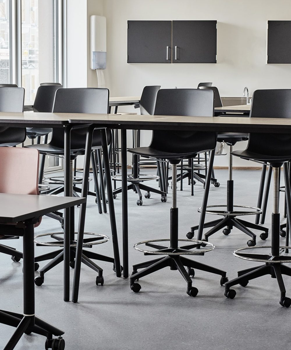 A classroom with counter height tables and chairs in it.