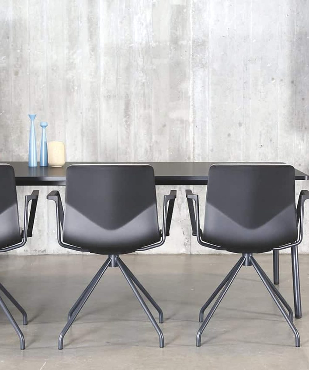 A black table with office screen divider and chairs in a room with a concrete wall.