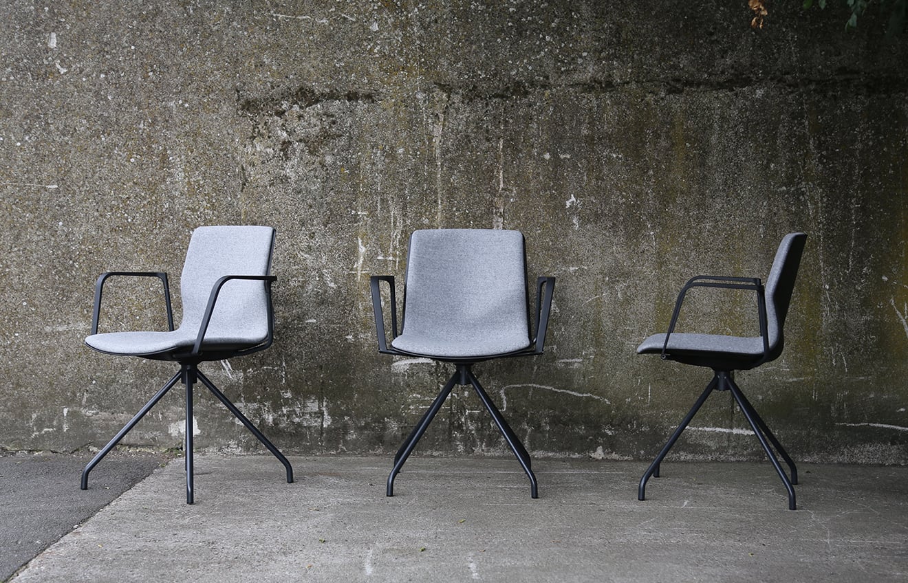 Three grey chairs against a concrete wall.