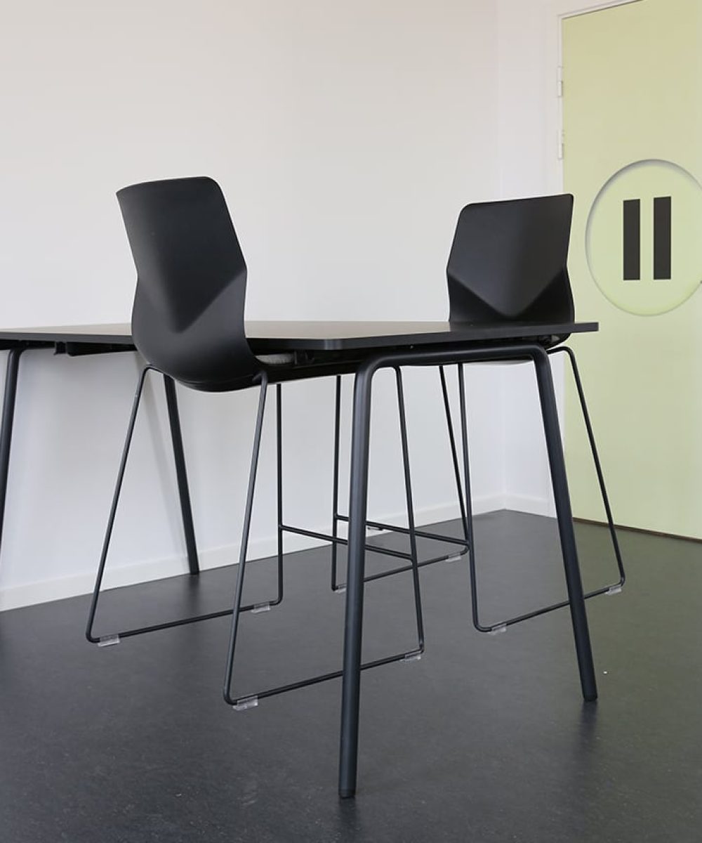 Two black counter chairs and a standing height table in an empty room.