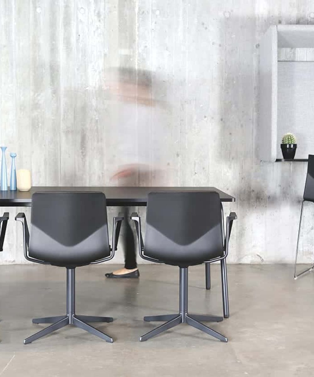 Four chairs and a table in a room with a wall mounted desk workstation on a concrete wall.