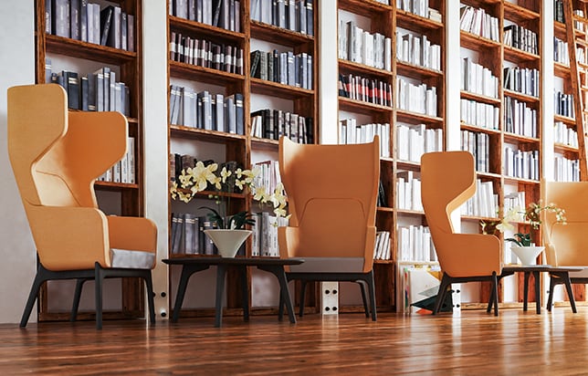 Four orange lounge chairs for offices in a library with bookshelves.