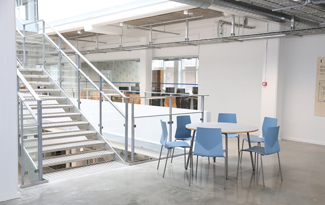 An office with a table and office desk chairs and a staircase.