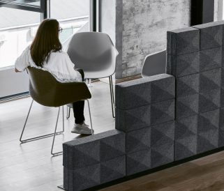 A woman sits in a chair in front of a gray wall of acoustic panels for offices