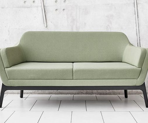 A green couch with black legs in front of a concrete wall.