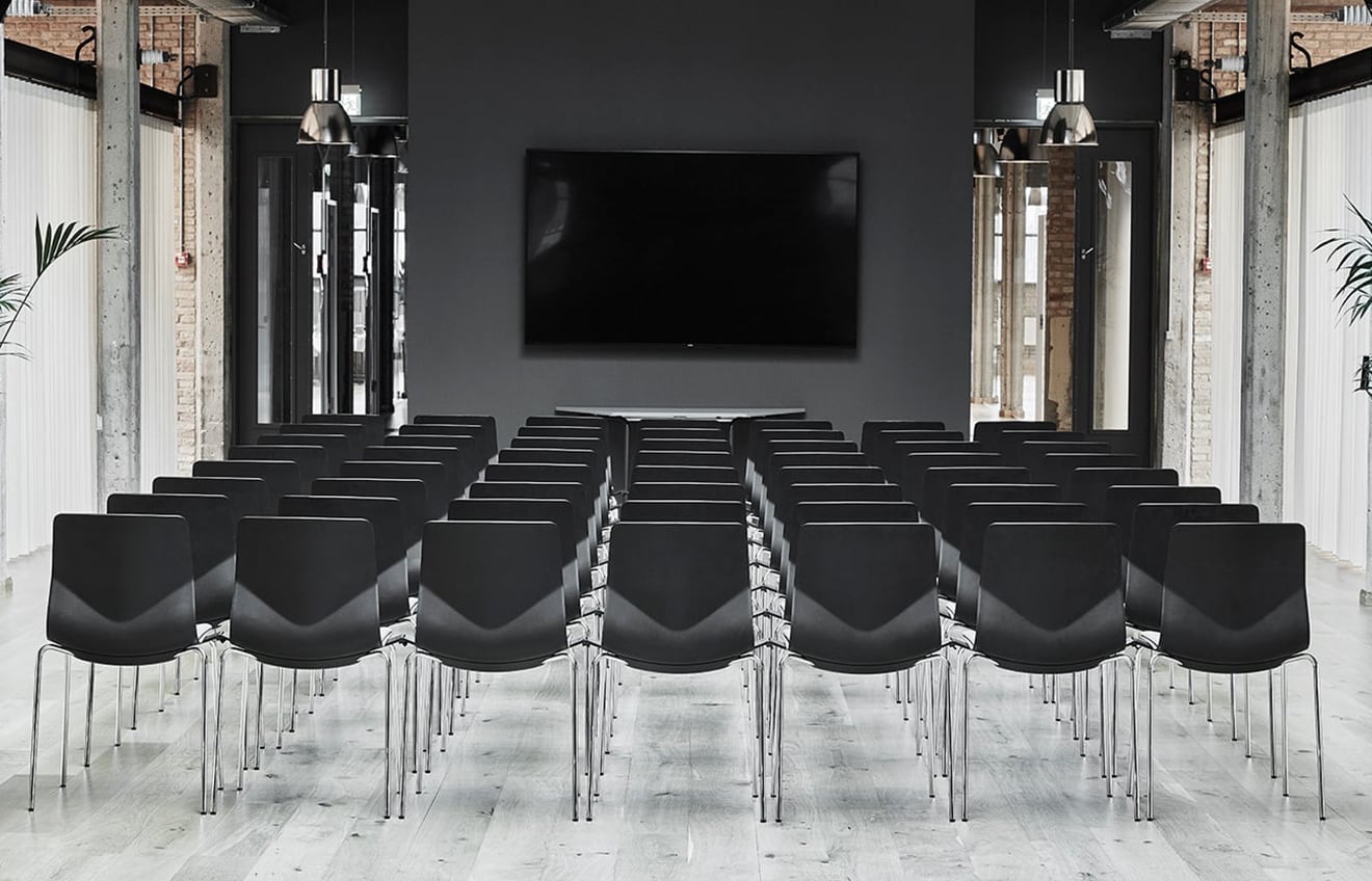 A room with rows of black chairs and a tv.