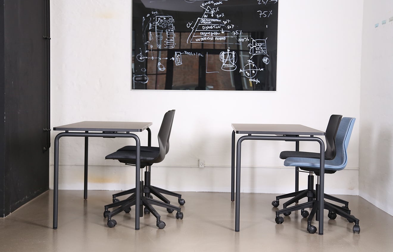 A black table and chairs in a room with a chalkboard.
