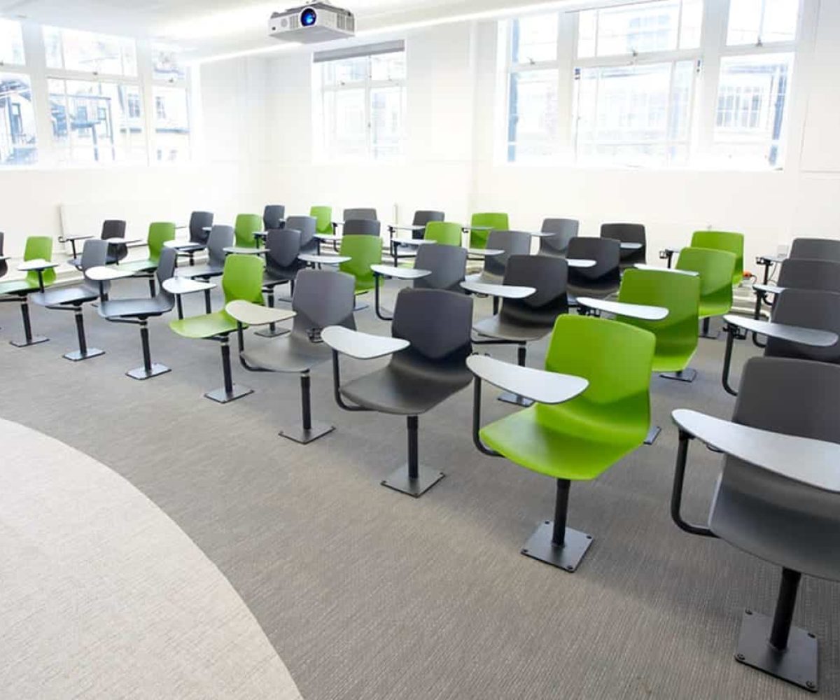 A classroom with green chairs with desk attached and a projector screen.