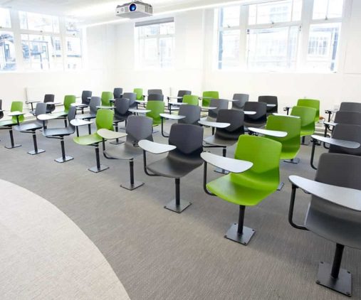 A classroom with green chairs with desk attached and a projector screen.