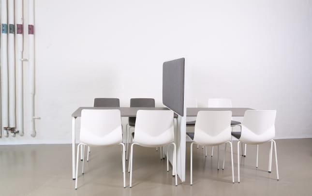 A white table with office screen dividers and chairs in an empty room.