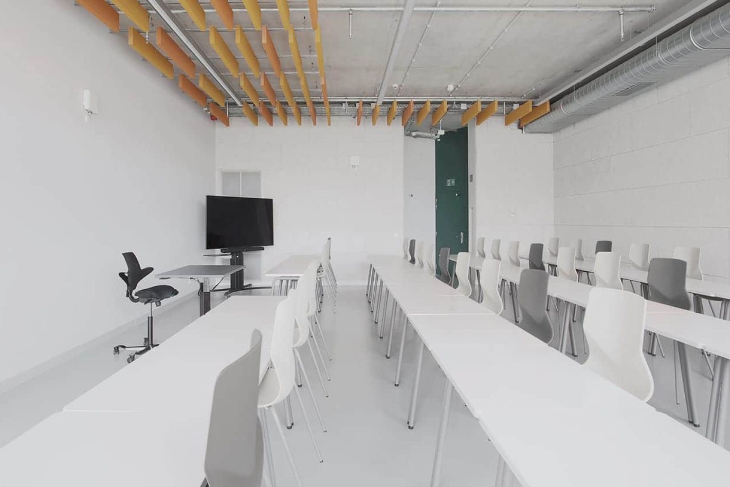 A group of office desk chairs and office tables in a lecture hall with a TV