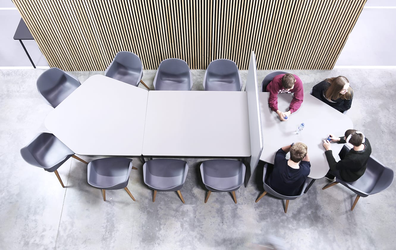 A group of people sitting around a table with an office screen divider in an office.