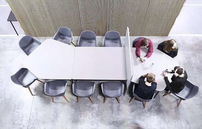 A group of people sitting around a table with an office screen divider in an office.