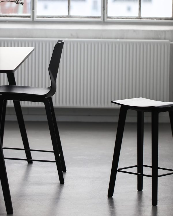 A dining table with two black counter height chairs and a stool in front of a window.