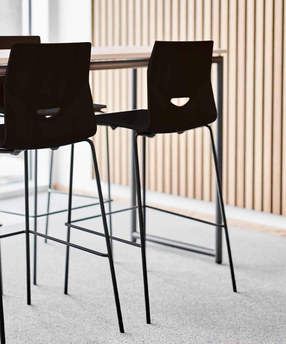 Four black counter chairs in an office with a wooden table.