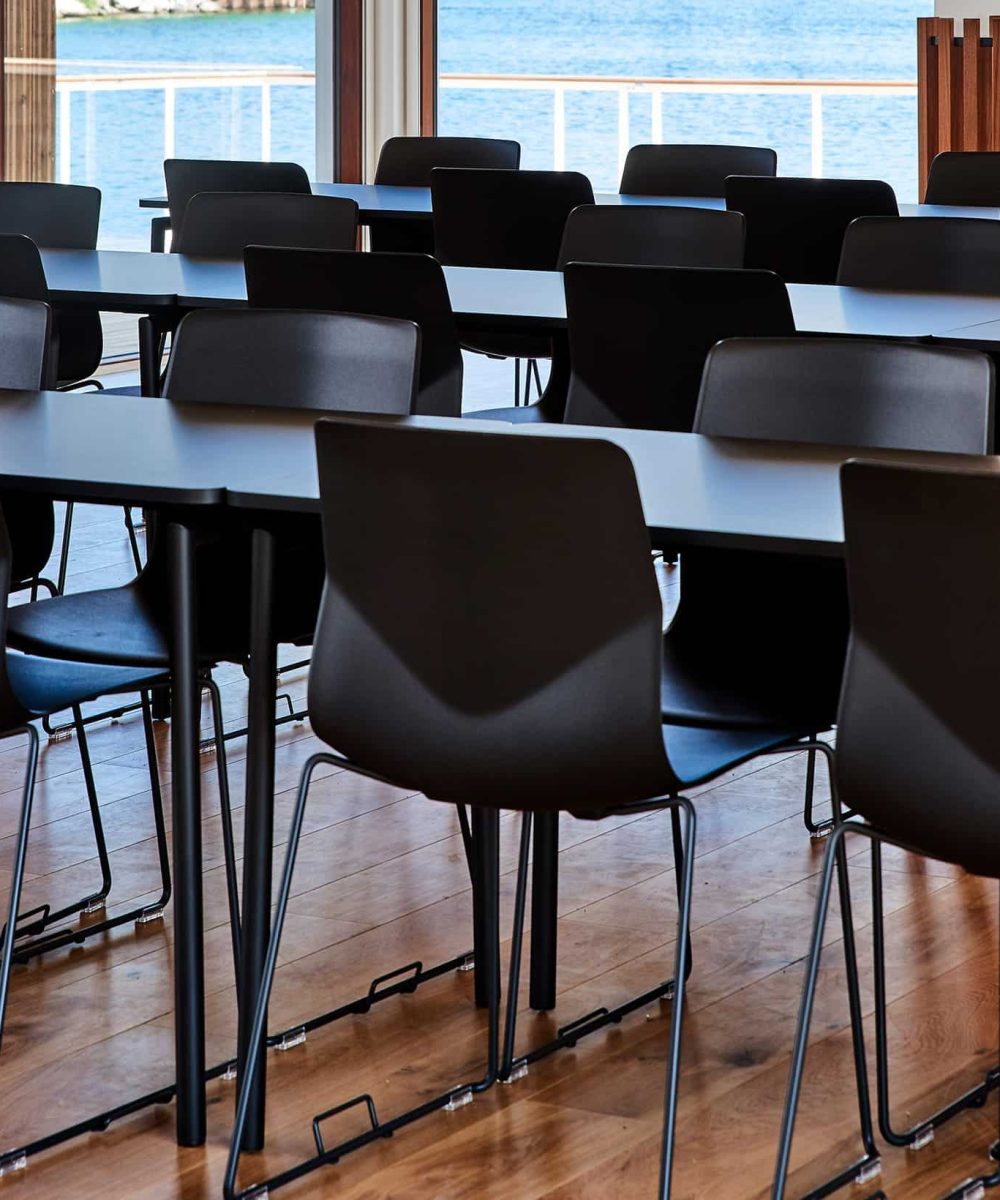 A long table with black chairs and a view of the water.