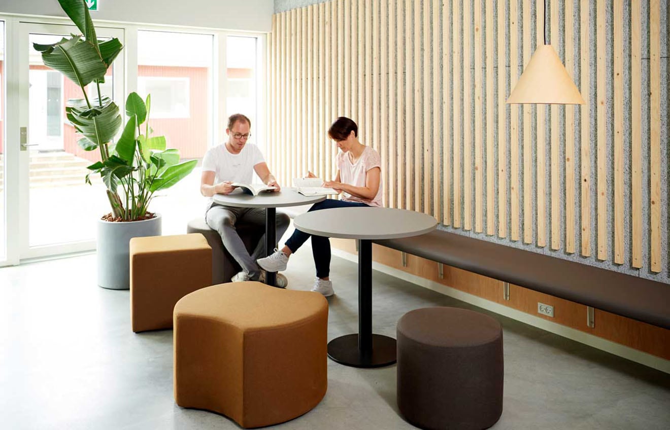 Two people sitting on a wall mounted bench at a table in an office.