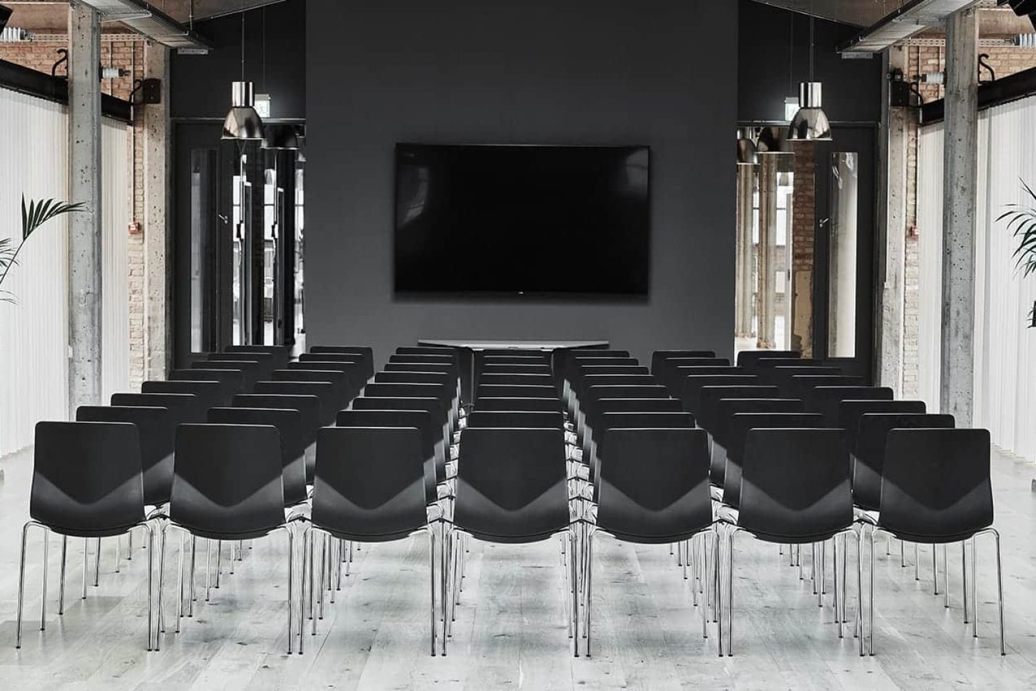 A large conference room with black office desk chairs and a large screen.