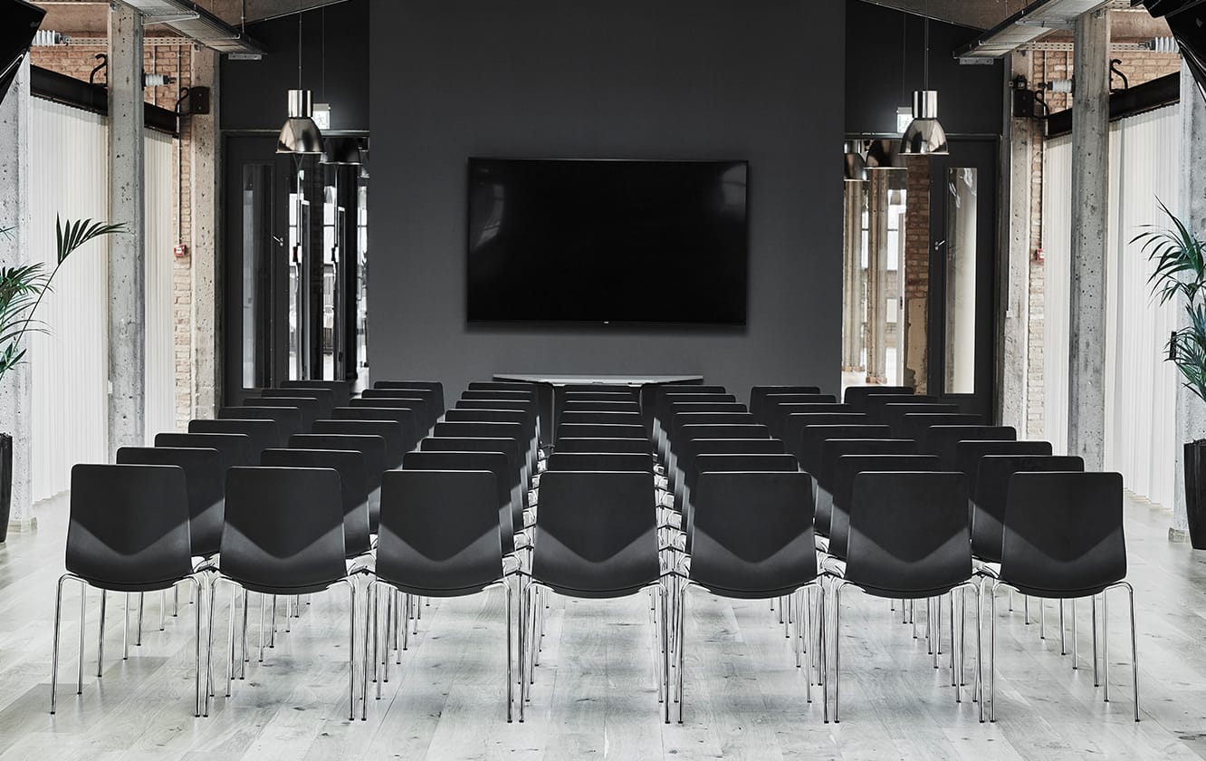A large conference room with black office desk chairs and a large screen.