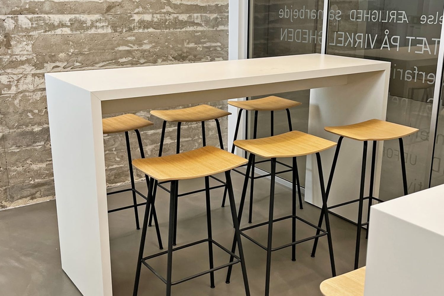 A white bar with wooden stools in front of a brick wall.