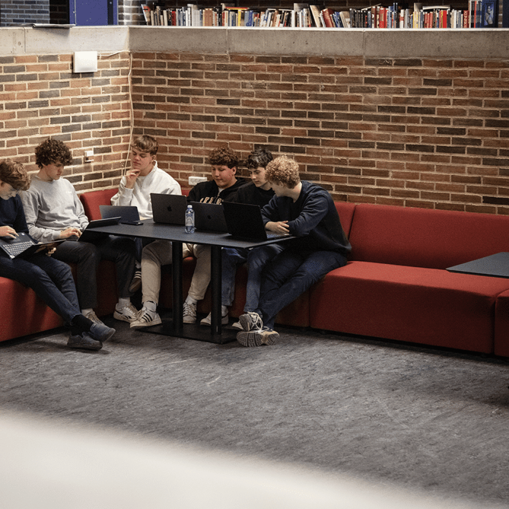 A group of people sitting on modular seating office sofas at desk workstations using laptops.