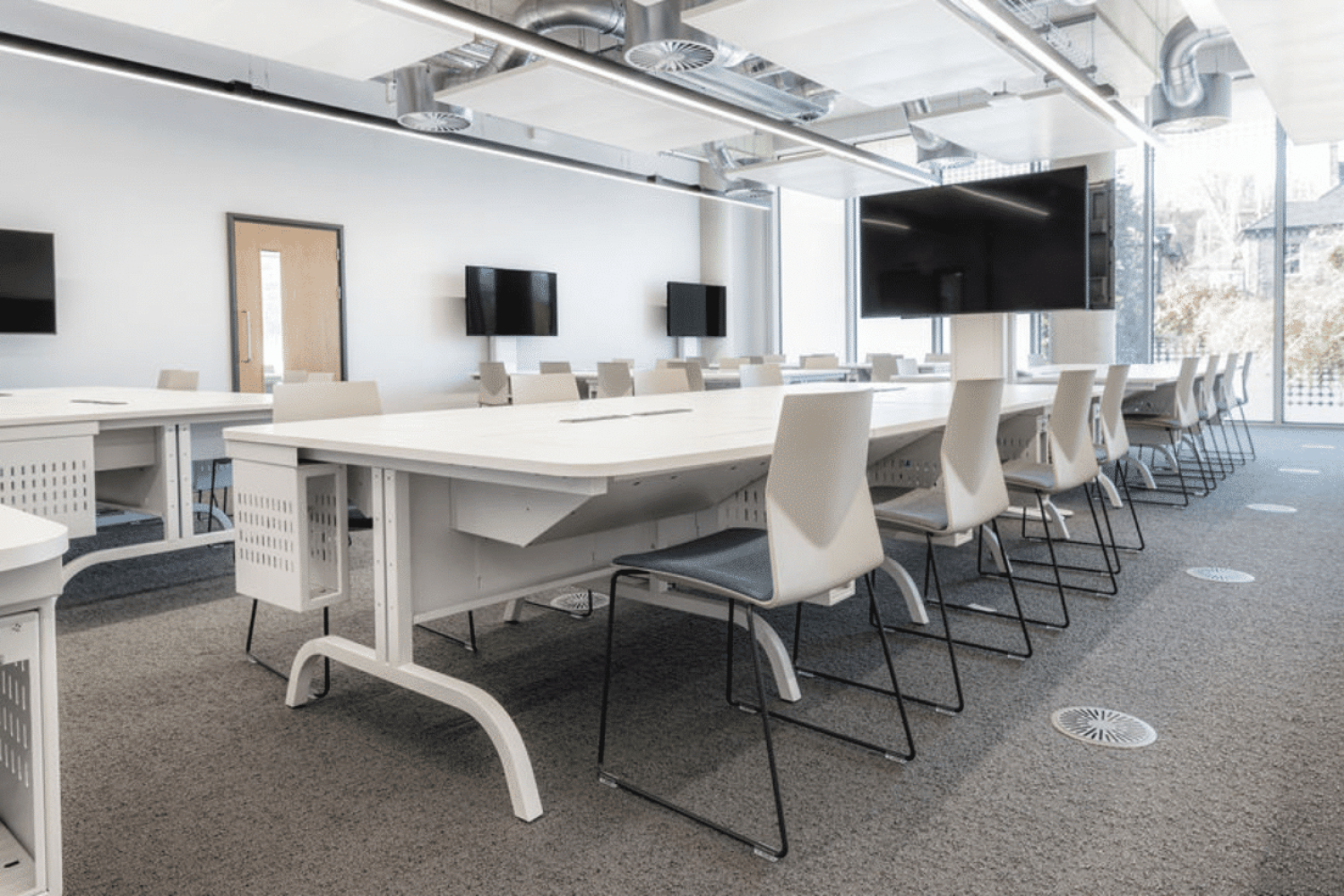 A classroom with tables and chairs and a tv with Ocee and Four Design office furniture as part of our student centre design for the University of Sheffield