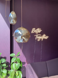 A room with a purple couch and a neon sign that says better together.