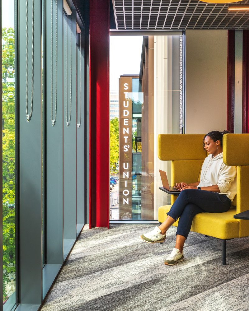 A woman is sitting on one of several yellow Ocee and Four Design office work booths.