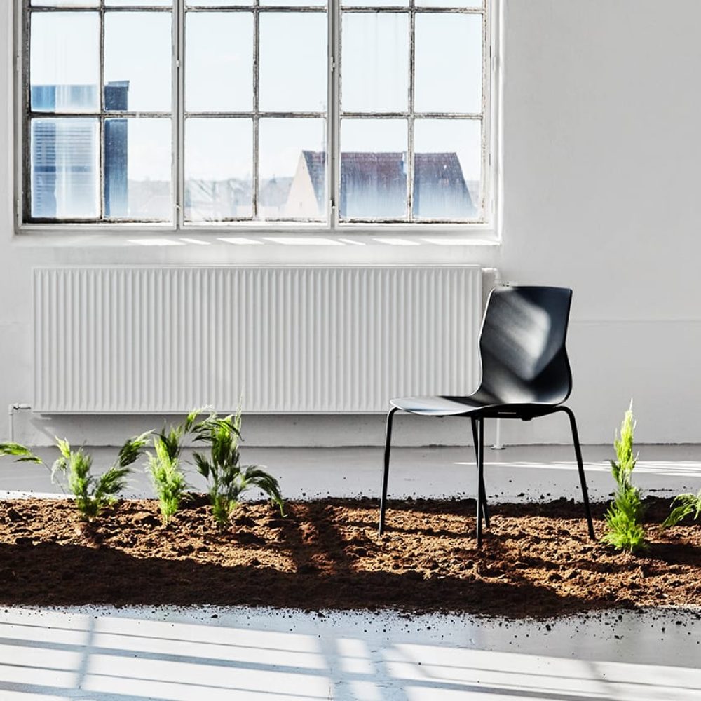 A black chair sits in the dirt next to a window.