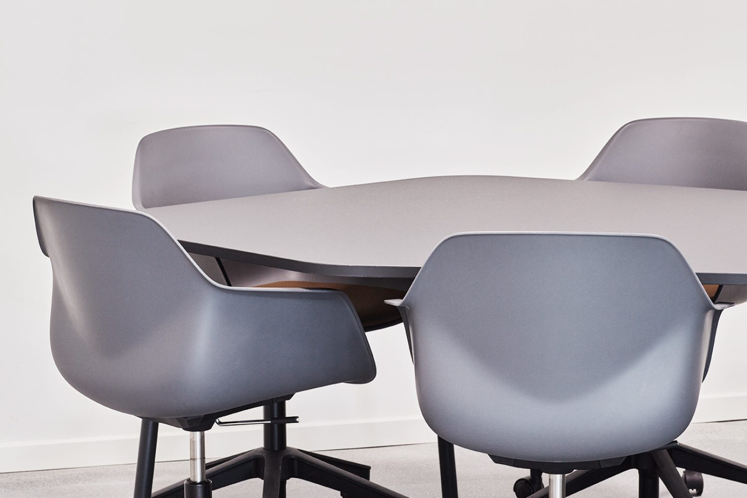 Four grey office desk chairs and a round table in an office.