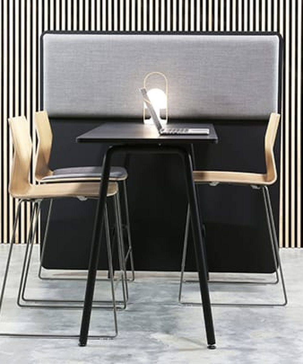 A black table against a office screen divider with an acoustic panel on it and chairs in a room with a striped wall.