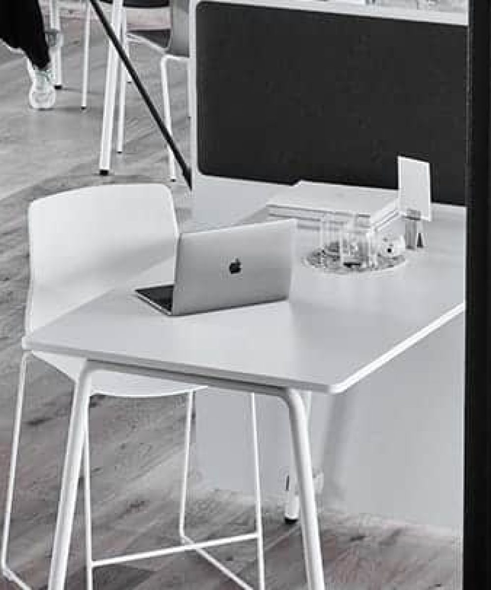 A white desk with an office screen divider in an office with a laptop on it.