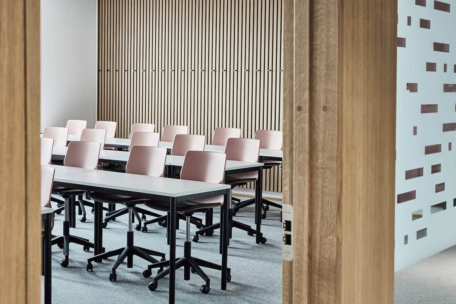 A conference room with pink office desk chairs behind office desks and wooden walls.