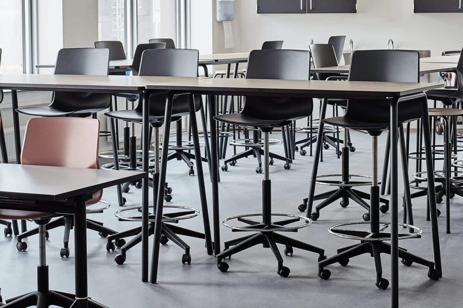 A classroom with a lot of office desk chairs and standing height tables.