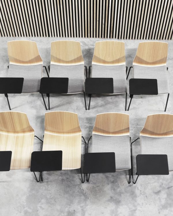 A row of wooden chairs with desk attached in a room with a wooden wall.