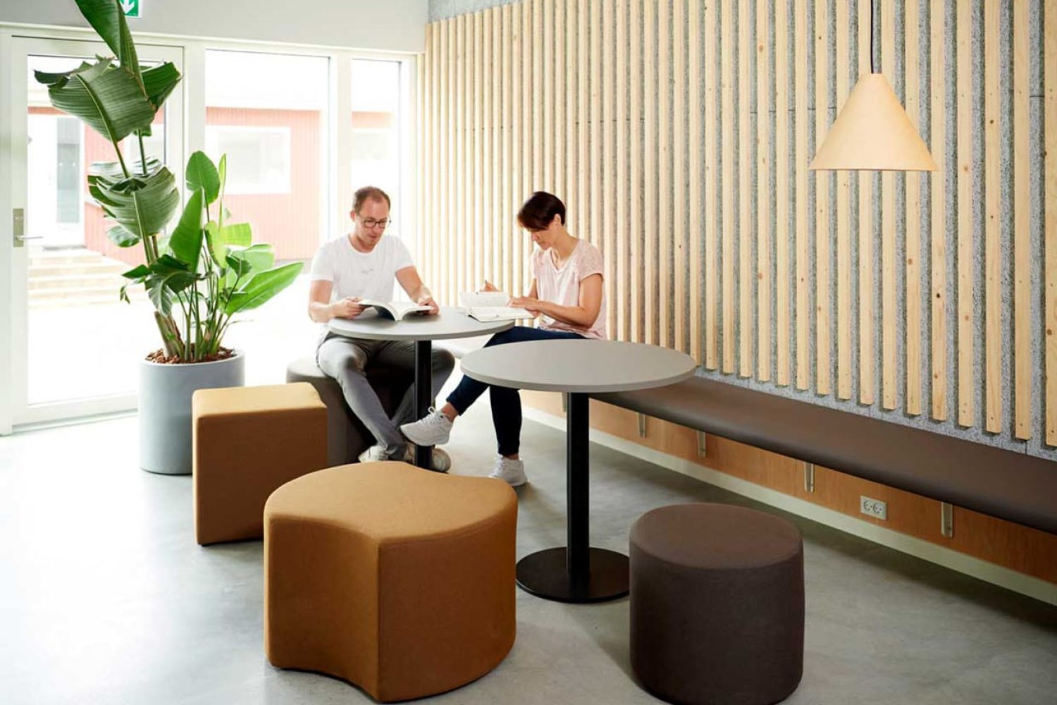 Two people sitting on a wall mounted bench at a table in an office.